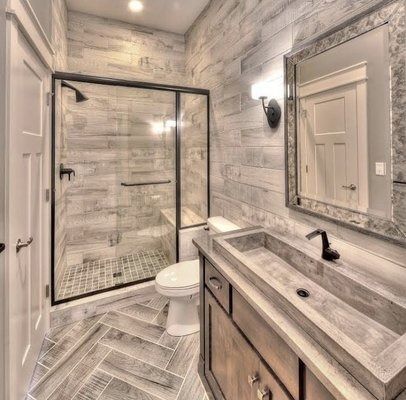 Bathroom with gray wood-look walls and herringbone floor. Shower, toilet, vanity with concrete sink, and a framed mirror.