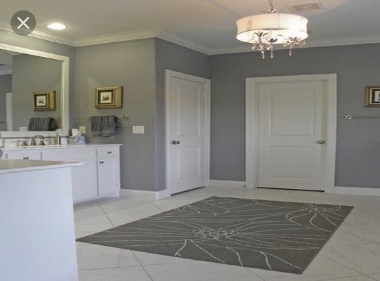 Gray-walled bathroom with white cabinets, doors, and floor. A gray rug sits in the center; a chandelier hangs from the ceiling.