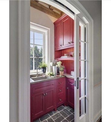 A small pantry with red cabinets, a sink, and a window, seen through a sliding glass door.