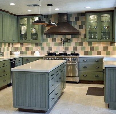 Green-toned kitchen with island, cabinets, and backsplash, stainless steel appliances, and pendant lights.