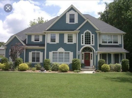 Two-story blue house with white trim, red door, and green lawn.