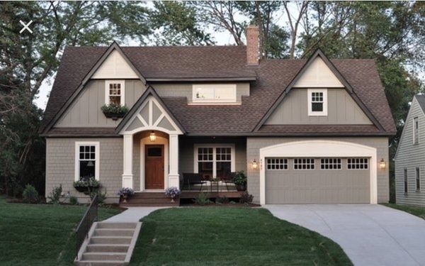 A gray house with brown roof, white trim, and a garage on a green lawn with a concrete driveway.