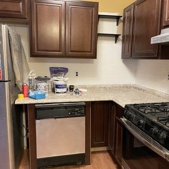 Kitchen with dark wood cabinets, stainless steel appliances, and countertops; paint supplies visible.