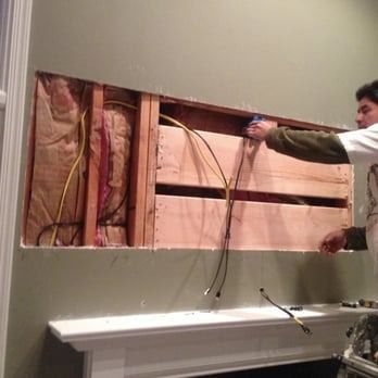 Man working on a recessed wall space, installing wiring and electrical components near a fireplace.