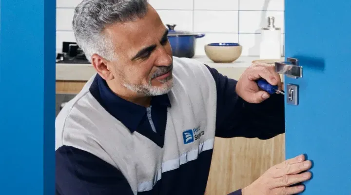 Um homem está consertando uma porta com uma chave de fenda em uma cozinha.