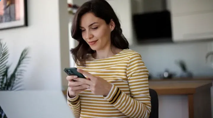 Uma mulher está sentada à mesa usando um celular.