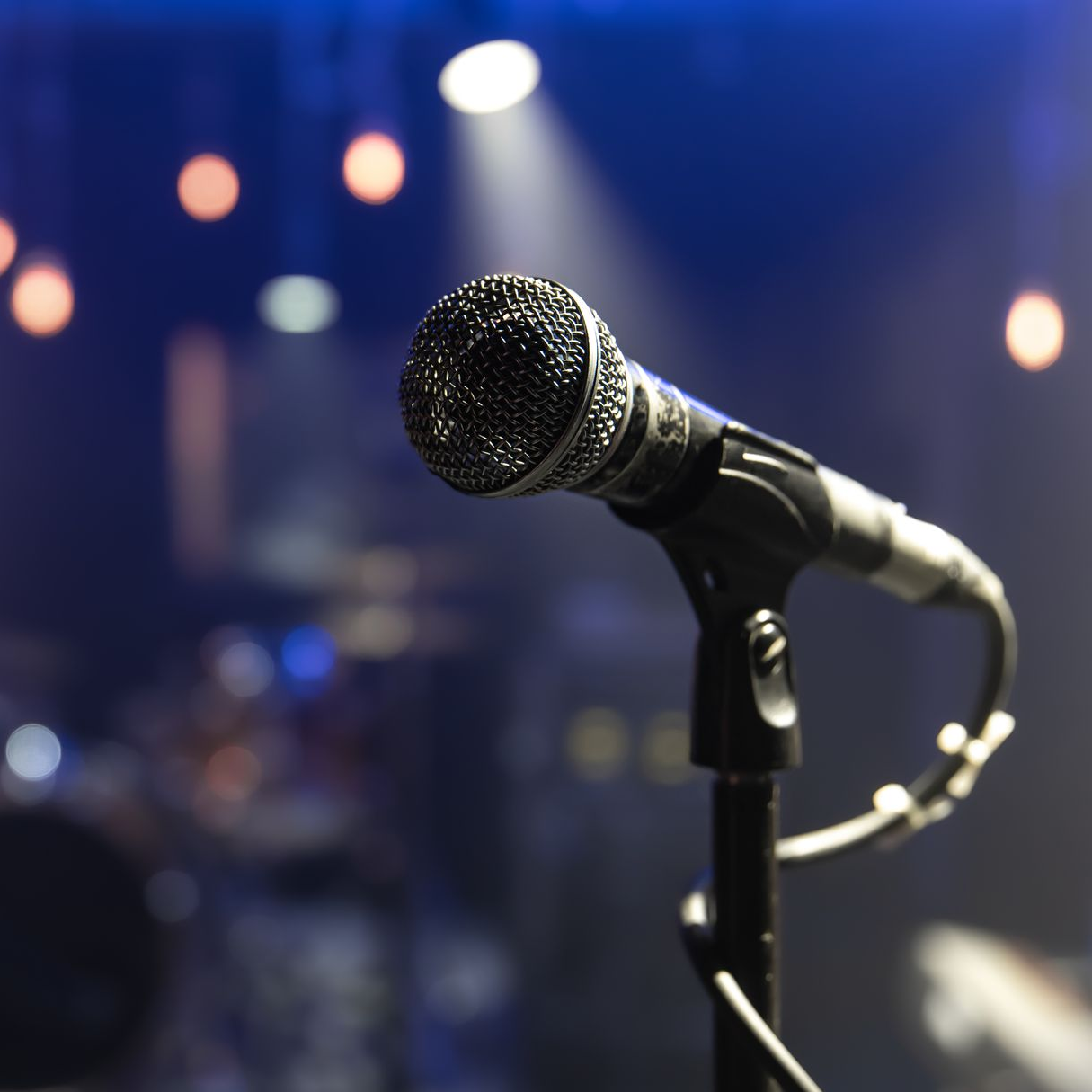 Micrófono en un soporte, escenario iluminado con un foco.