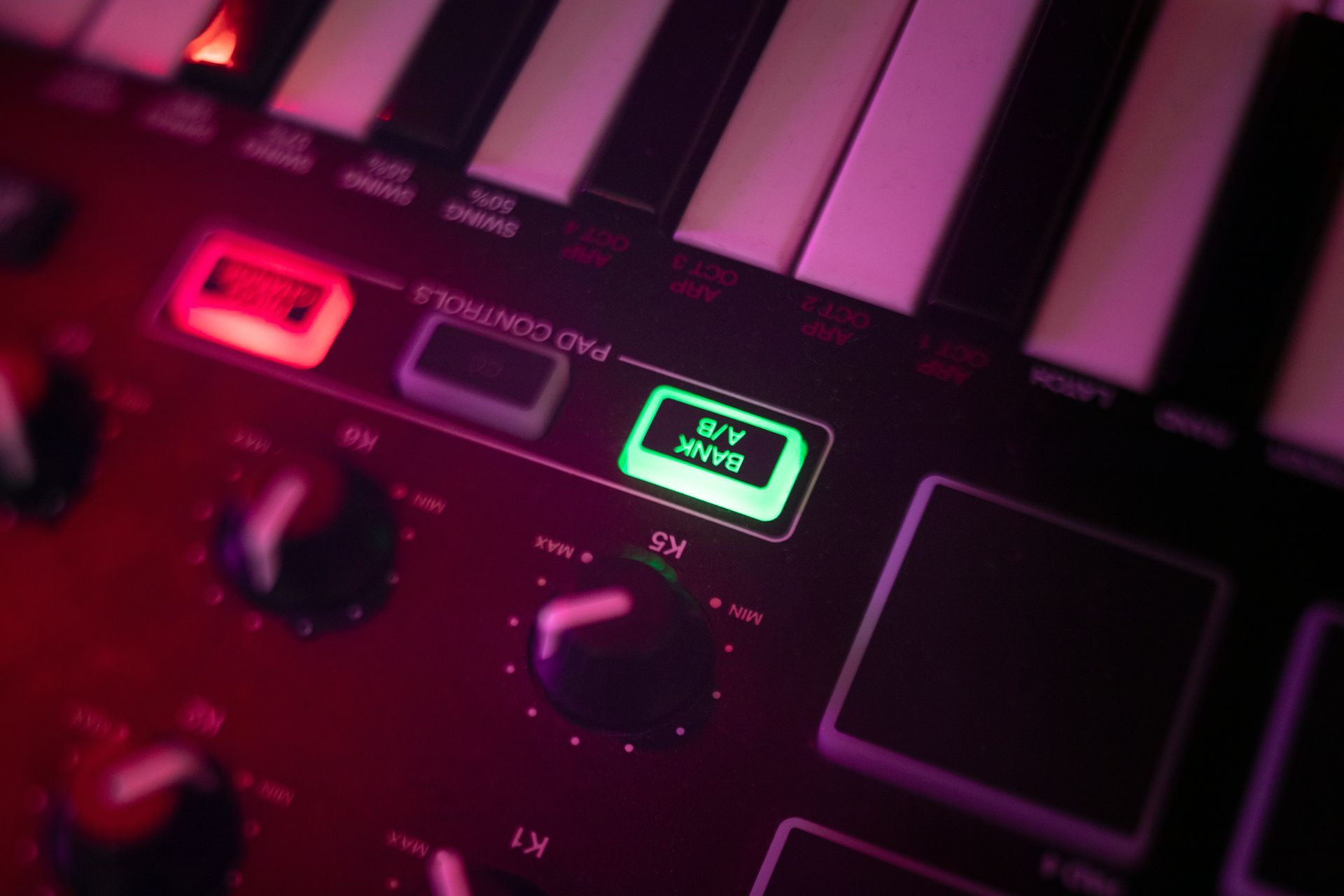 Primer plano de un controlador de teclado MIDI rojo con botones verdes y rojos iluminados y teclas negras.