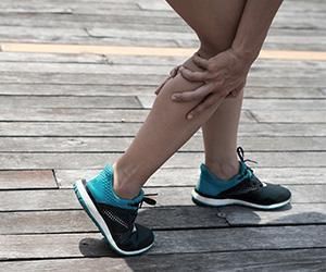 A woman is holding her leg in pain on a wooden deck.