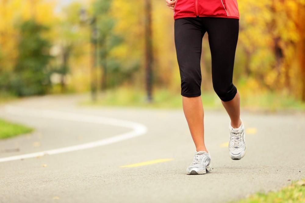 A woman is running down a road in a park.