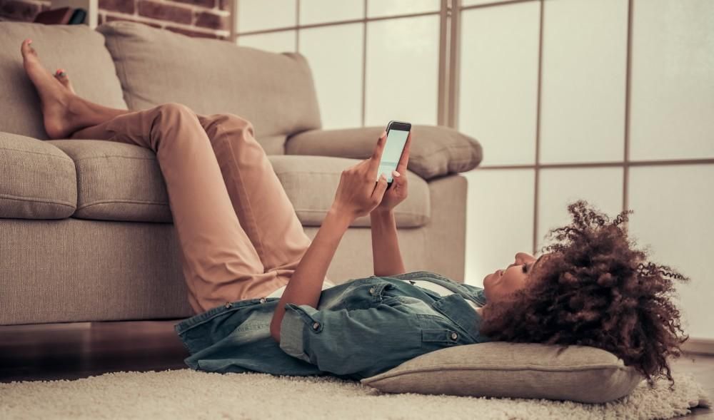 A woman is laying on the floor using a cell phone.