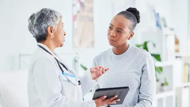 A doctor is talking to a patient while holding a tablet.