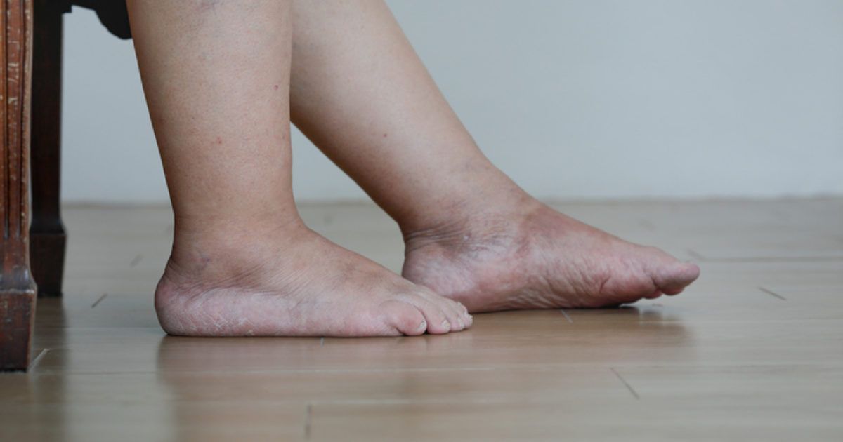 A person 's bare feet are sitting on a wooden floor next to a chair.