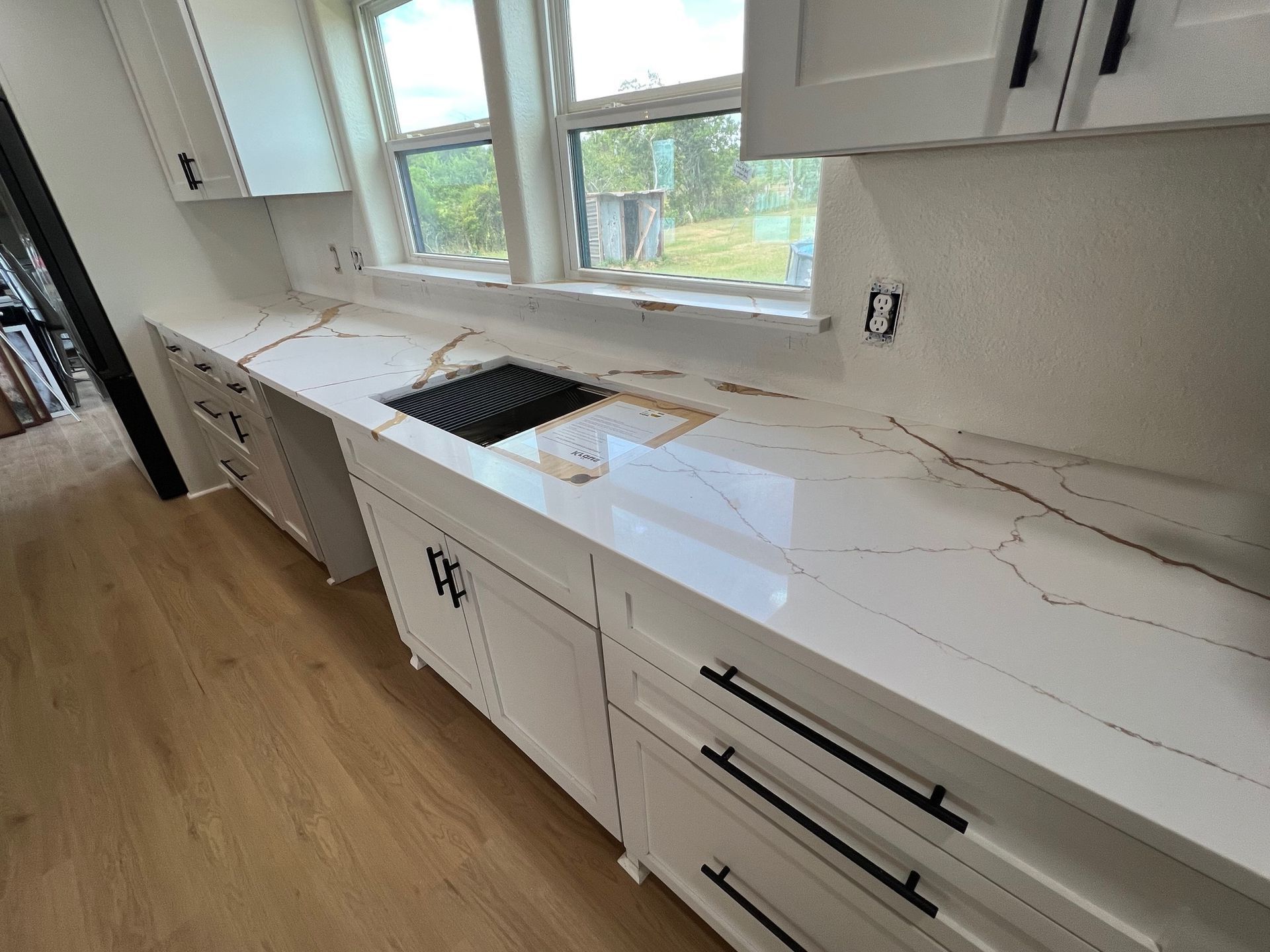 White kitchen cabinets with black hardware and a white countertop with gold veining, a cooktop is visible.