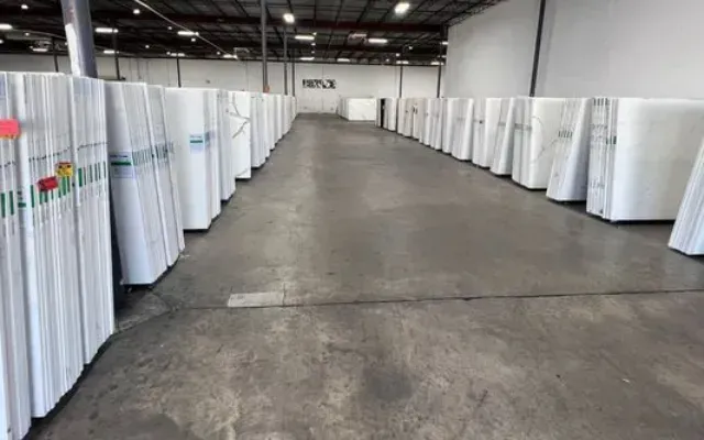 Rows of white boards stacked in a warehouse with a concrete floor.