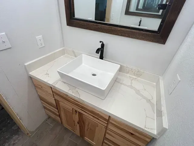 Bathroom vanity with a white rectangular sink, wooden cabinet, and quartz countertop. Black faucet and mirror.