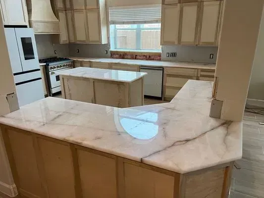 Kitchen with light-colored cabinets, white marble countertops, and a central island, still under construction.