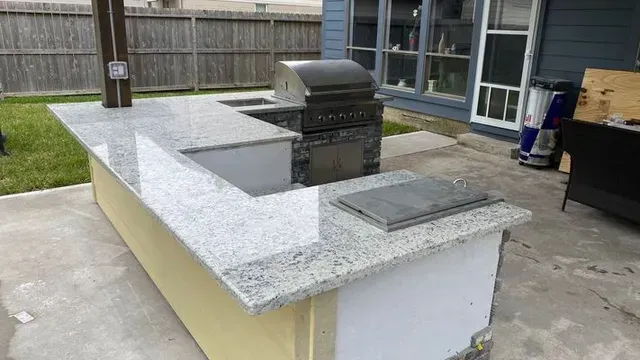 Outdoor kitchen with granite countertop, grill, and sink. Yellow base with a wooden post.