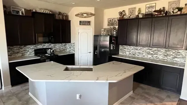 A kitchen with dark cabinets, white countertops, and a gray island.