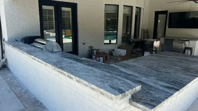 Outdoor kitchen with a granite countertop, grill, and white brick.