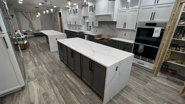 Modern kitchen with two islands, gray cabinets, white countertops, and wood-look flooring.