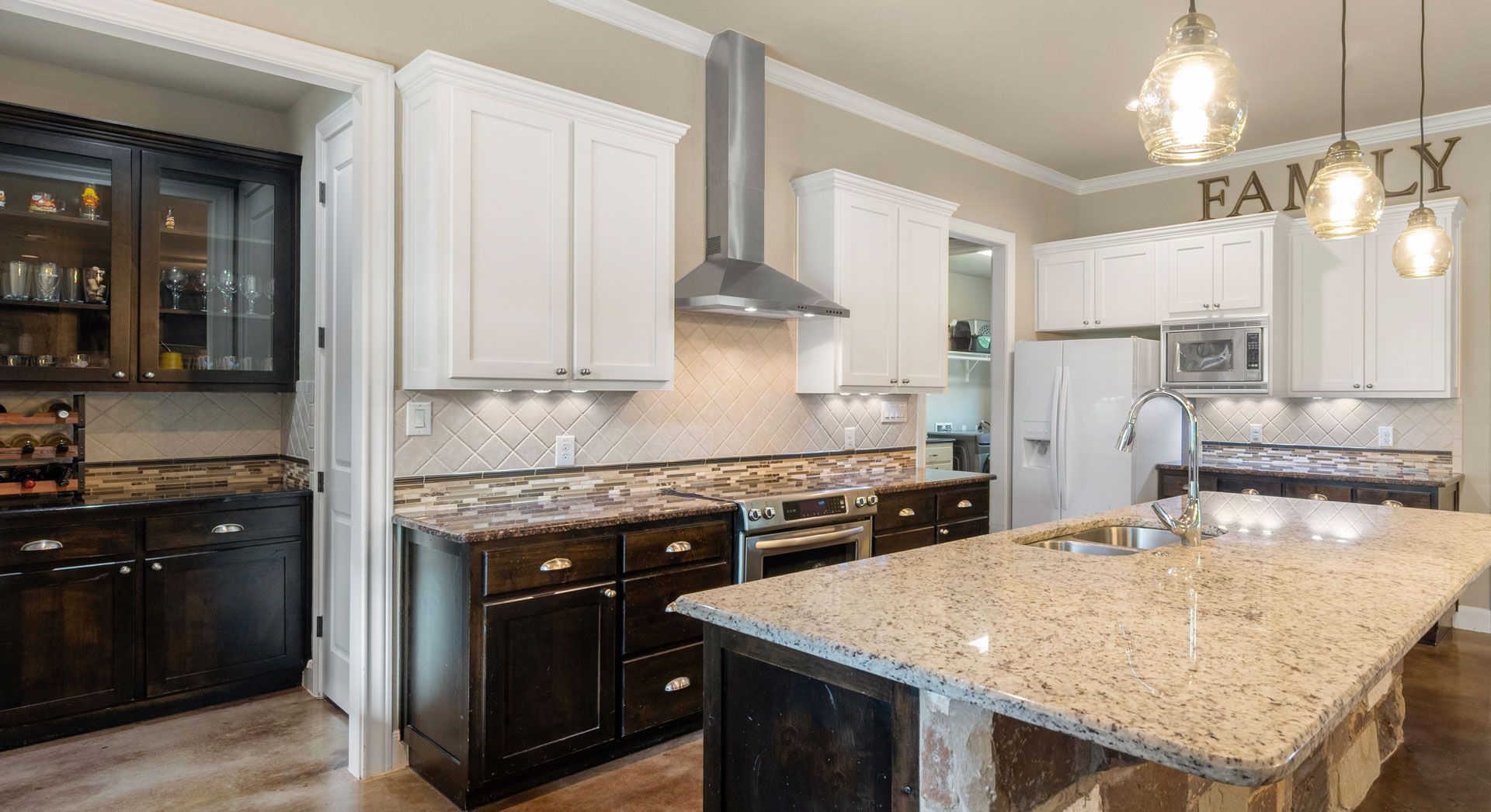 Bright modern kitchen with white cabinets, dark appliances, granite island, and dining area sign reading “FAMILY”