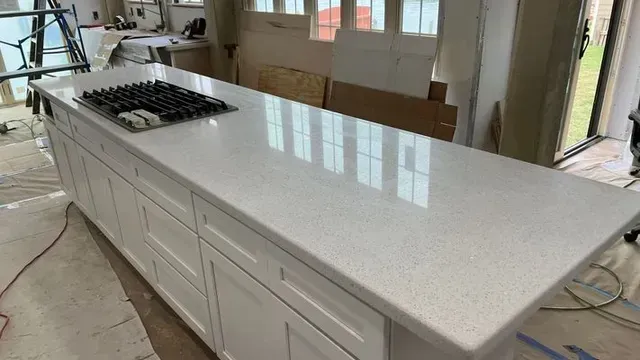 White kitchen island with gas stovetop, quartz countertop, and white cabinets during renovation.