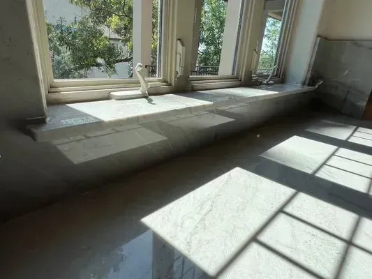 Sunlight streams across a marble windowsill, highlighting the window and a tiled floor.