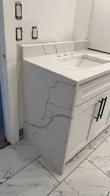 White bathroom vanity with marble-like countertop and cabinet, black hardware.