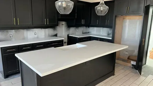 Black kitchen cabinets with white countertops and island, pendant lights overhead.
