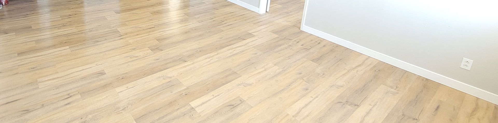 Light wood flooring with a white-painted wall and baseboard.