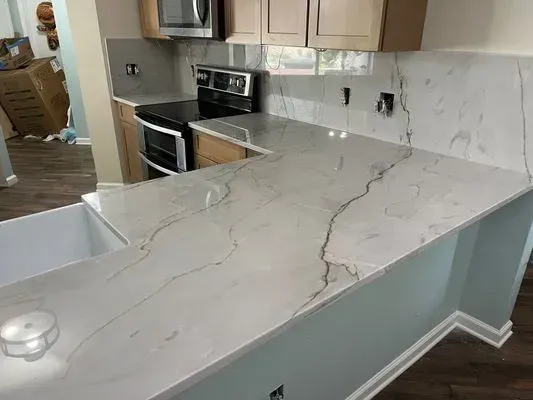 A light-colored kitchen countertop with a marble-like pattern. Cabinets and appliances are also visible.