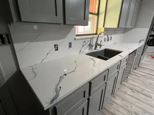 Gray cabinets and white countertops with dark veining in a kitchen; sink and faucet visible.