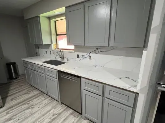 Gray kitchen cabinets and white countertop with a stainless steel dishwasher.