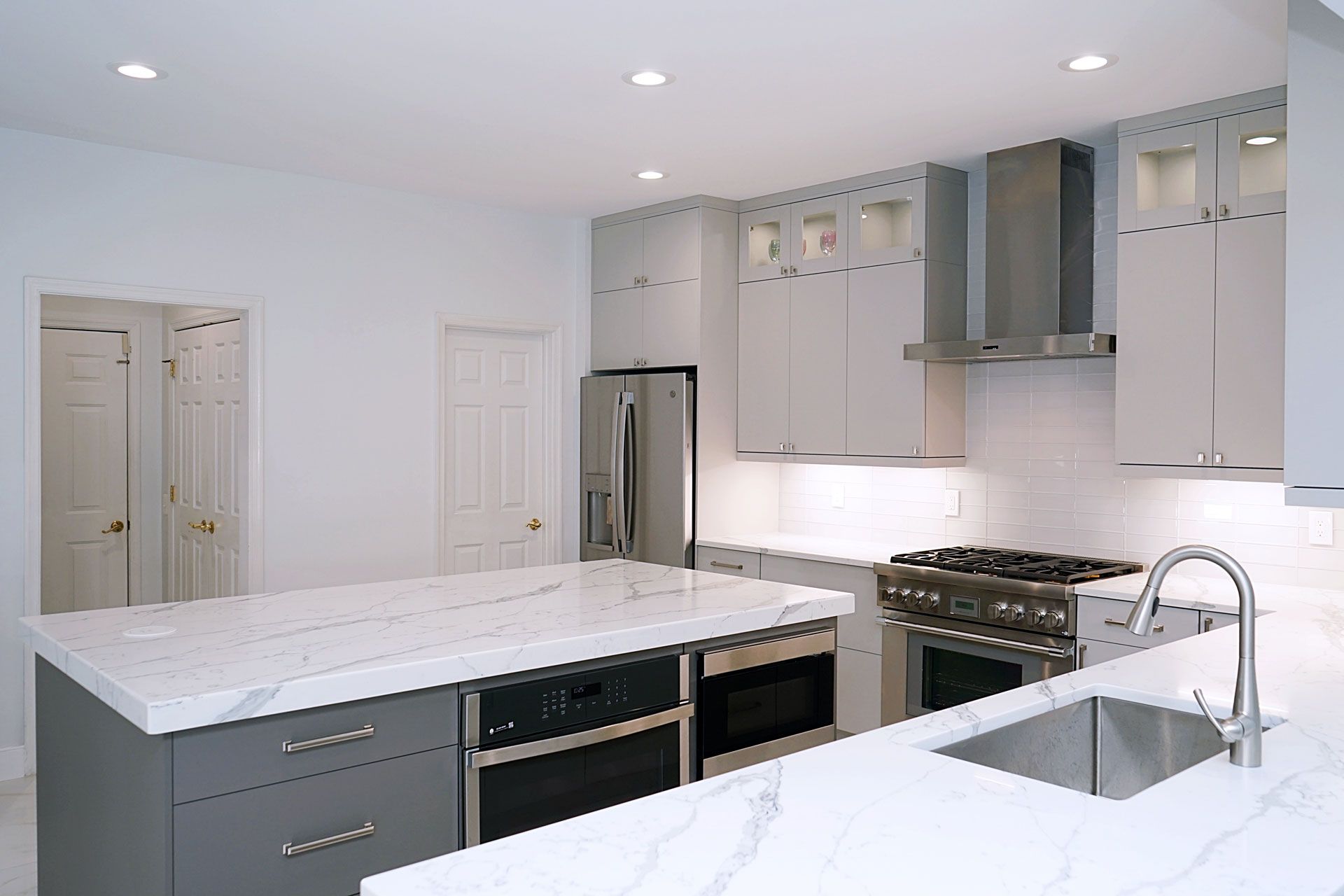 Bright modern kitchen with white countertops, gray cabinets, stainless steel appliances, and a large island.
