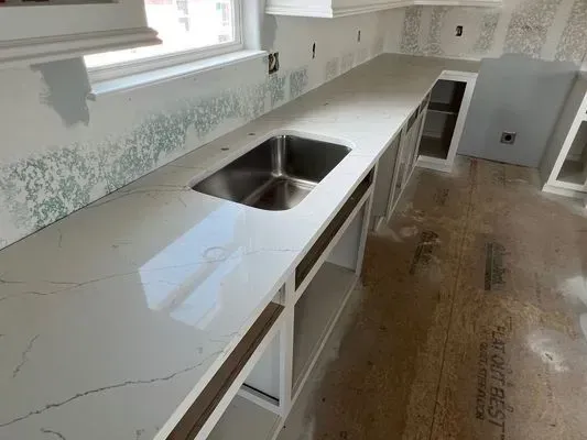 A kitchen countertop with a stainless steel sink, under-cabinet space, and a window in the background.