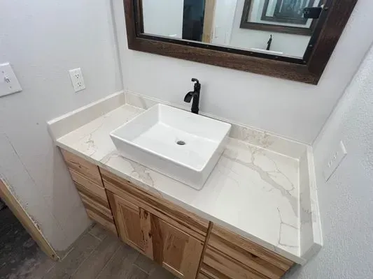 Bathroom vanity with a white rectangular sink, black faucet, and light wood cabinets, under a mirror.