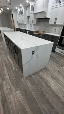 Modern kitchen with a large white marble island, dark gray cabinets, and light wood-look tile flooring.