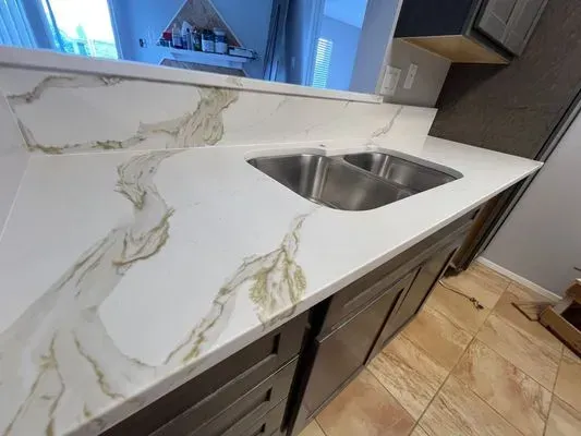 Kitchen with white countertop, gold veining, stainless steel sink, and dark brown cabinets.
