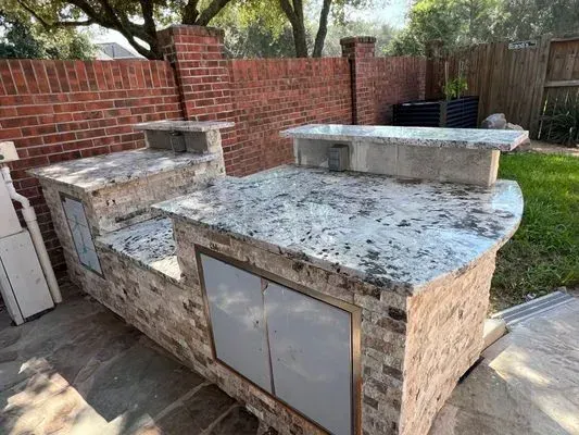 Outdoor brick and granite countertop bar with two sections, cabinets, and a raised countertop.