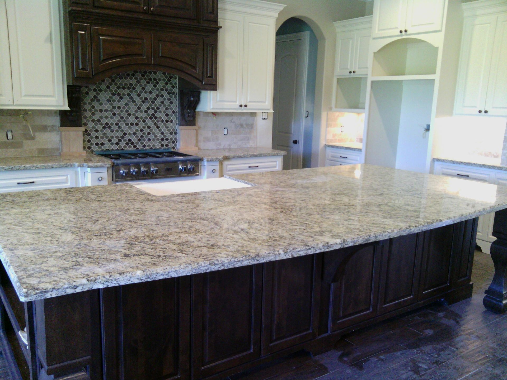Kitchen with large island, dark cabinets, granite countertop, white upper cabinets, and a stove.