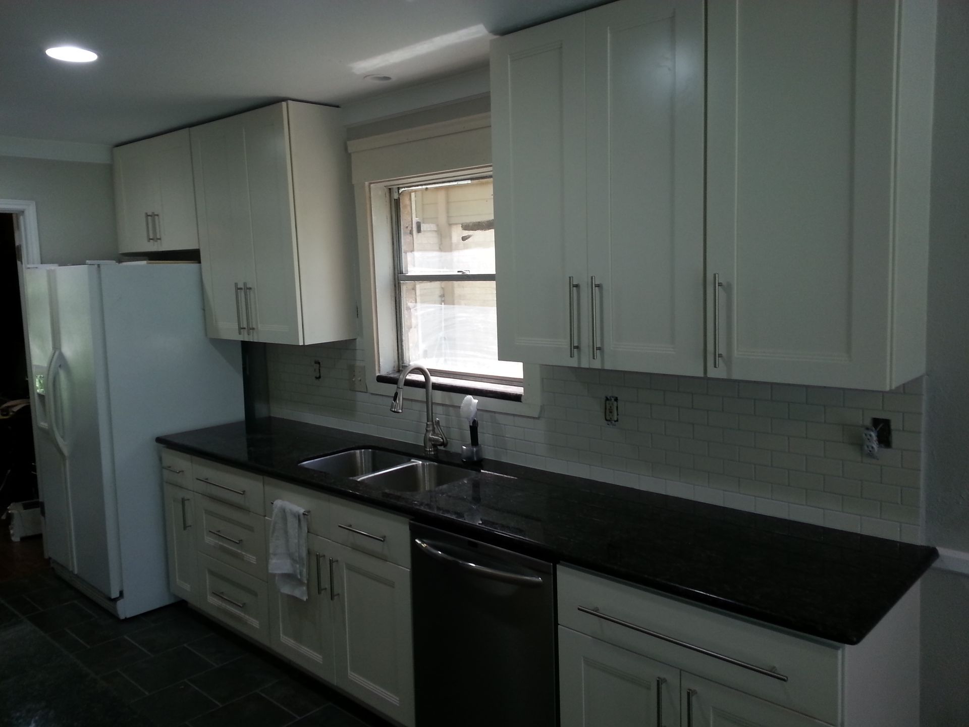 Kitchen with light cabinets, black countertops, and a window above the sink.
