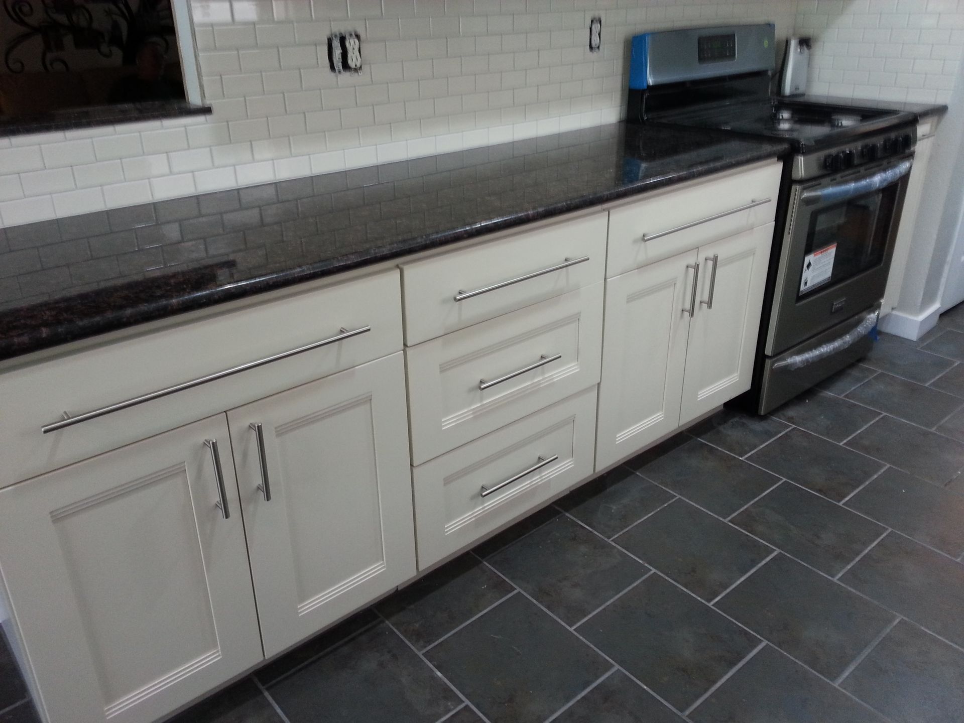 Kitchen with light gray cabinets, black countertop, stainless steel oven, and dark tiled floor.