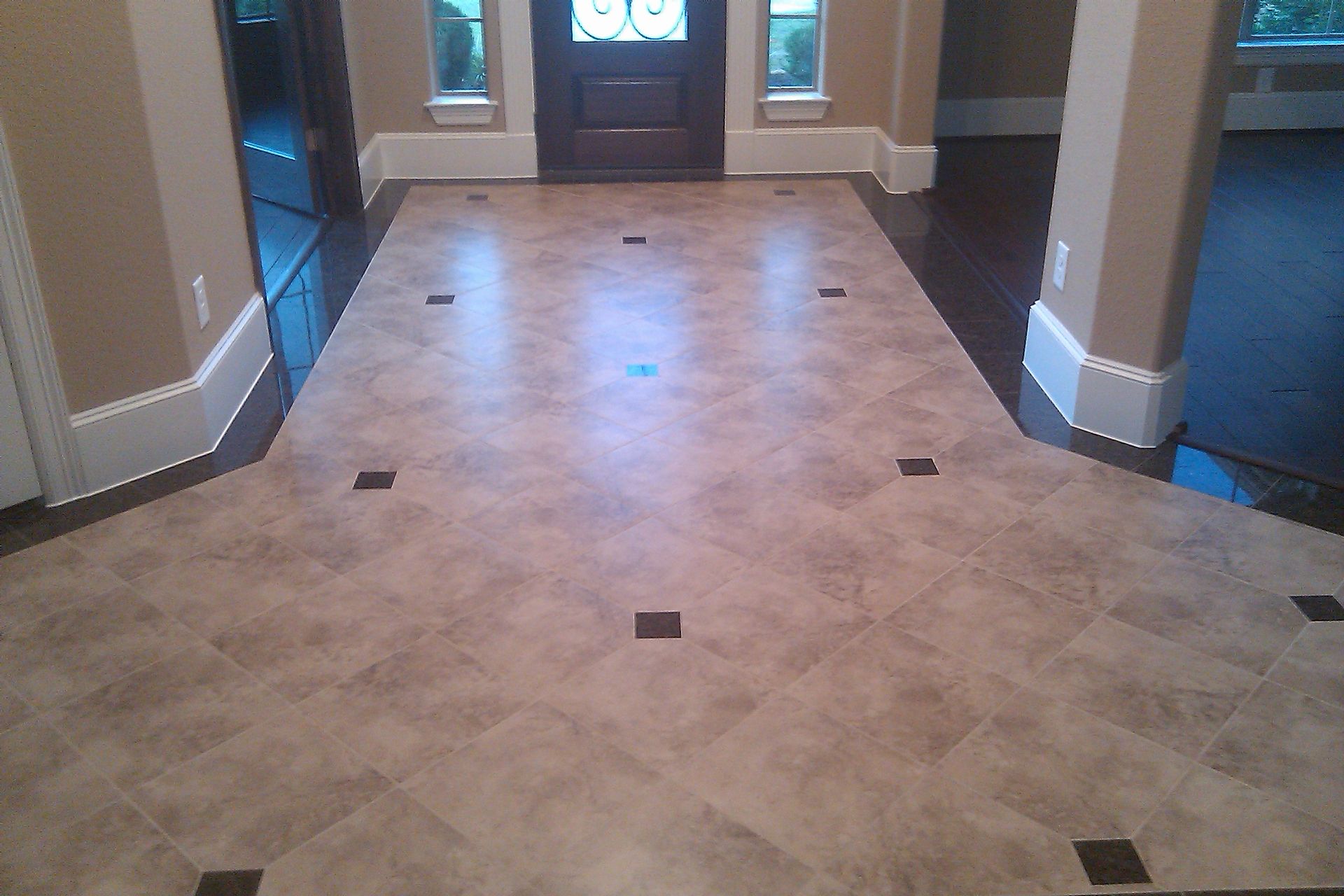 Foyer with light tan tile floor and dark brown border, accented with dark square tiles.
