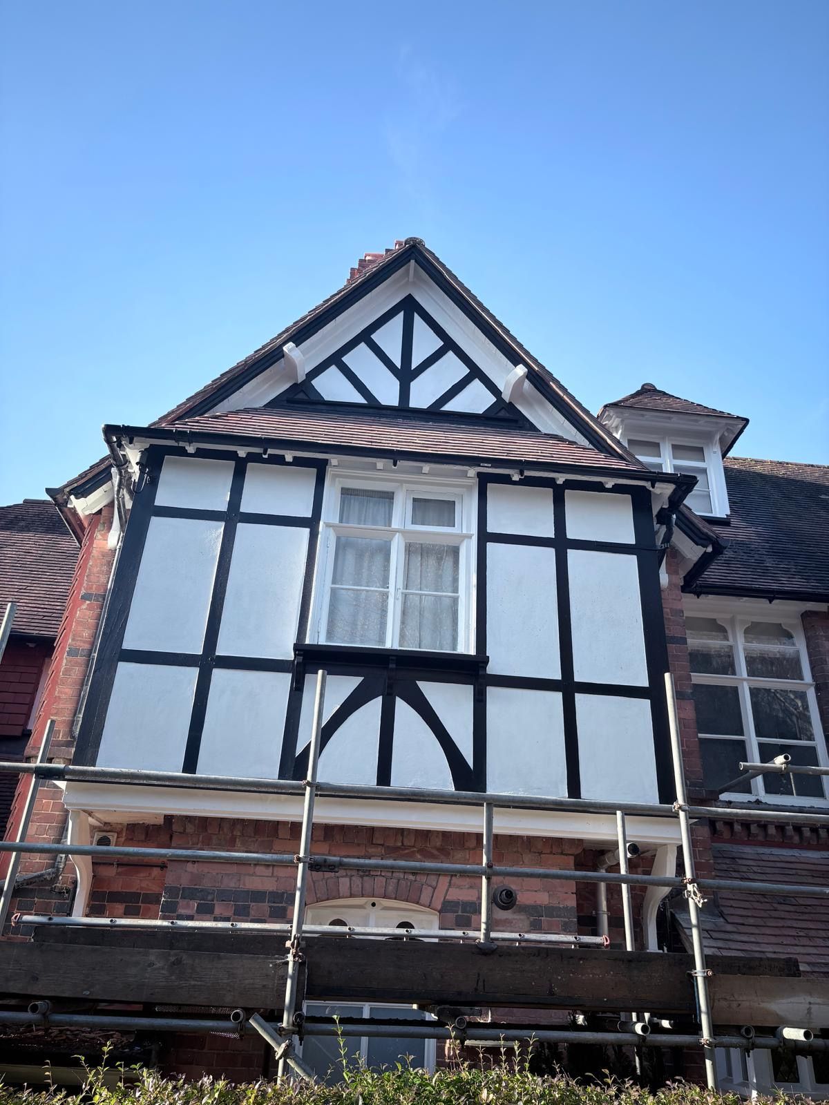 Tudor-style building with white and black detailing, a window, and scaffolding below, on a sunny day.