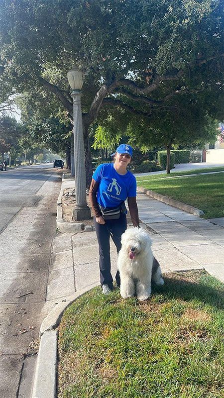 A small white dog is walking on a leash on a sidewalk.