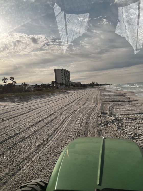 Tractor smoothing sand on a beach near a building under a cloudy sky.
