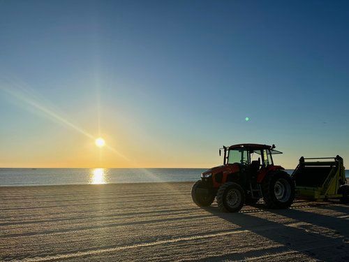 Tractor on a beach at sunset, sea in the background, blue sky.