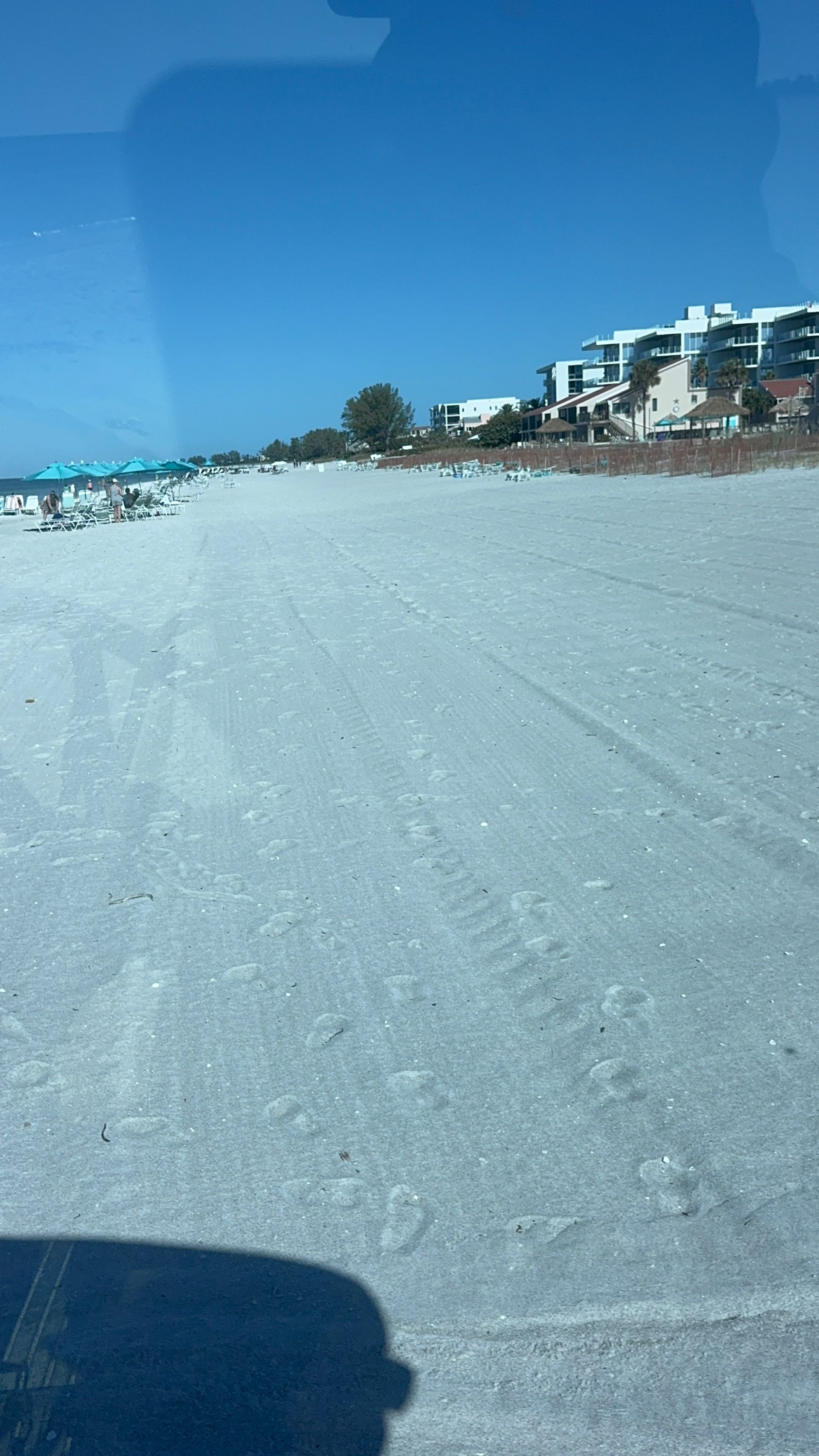 White sand beach with a clear blue sky and condos in the distance.