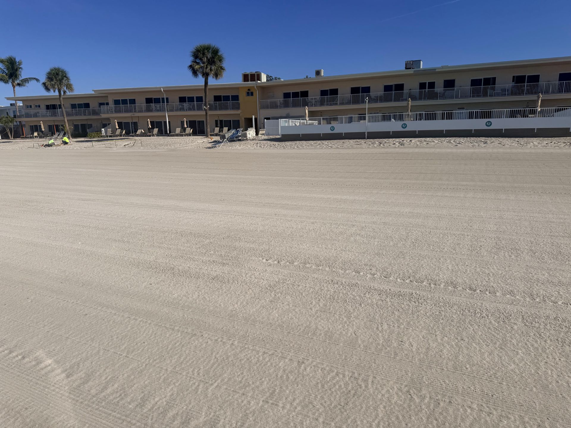 Beachfront hotel with balconies, light tan sand, and clear blue sky.